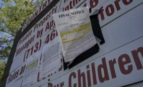 A "FINAL NOTICE" eviction letter, highlighted in yellow, is posted on a large sign that reads "Private Property" with a contact phone number in bold red text. Several other official notices are also stapled to the sign. The background shows green tree branches under daylight.