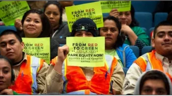 The image depicts a group of individuals in a meeting or assembly setting, holding up signs that read "FROM RED TO GREEN PARK EQUITY NOW!" This suggests they are part of an advocacy group or a public gathering focused on promoting equitable access to parks and green spaces. Some individuals are wearing fluorescent safety vests, which could indicate they are part of a workforce or volunteering group. The audience seems engaged and concerned about the issue of park equity.